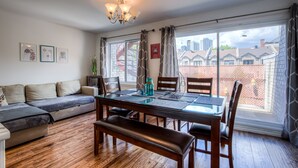 Un comedor con una mesa de vidrio, sillas de madera y un banco. Hay un sofá con cojines y un mueble bajo con una planta.