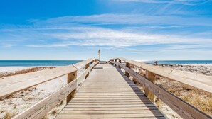 Une promenade en bois menant à une plage, avec un drapeau au bout.