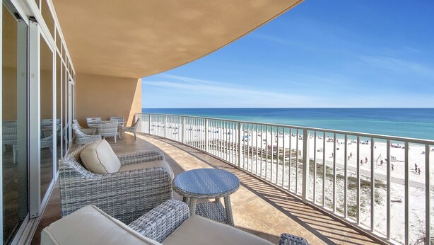 Un balcon agrémenté de meubles en osier, une vue sur la plage et un ciel dégagé.
