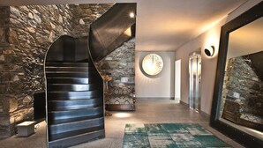 A modern interior with a spiral staircase, stone walls, and a large round wall clock.
