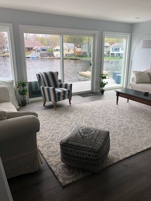 A living room with a large window, a striped armchair, a patterned ottoman, and a sofa. - Lake House, ONE HOUR from NYC (Newburgh)