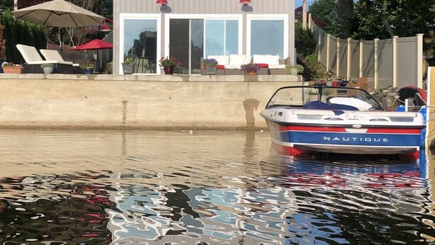 Una casa de dos pisos con un porche cubierto y un bote amarrado en el agua.