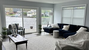 Amplia sala de estar con un gran ventanal con vistas a una masa de agua, un sofá azul oscuro, un sillón estampado y una mesa de centro de madera.