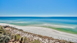 Ein Strand mit einer Holzpromenade, die zum Ufer führt, bewölkter Himmel und ruhige Wellen.