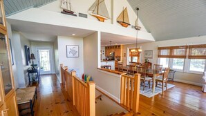 Un amplio espacio de sala con piso de madera, un techo alto y vista a la cocina.
