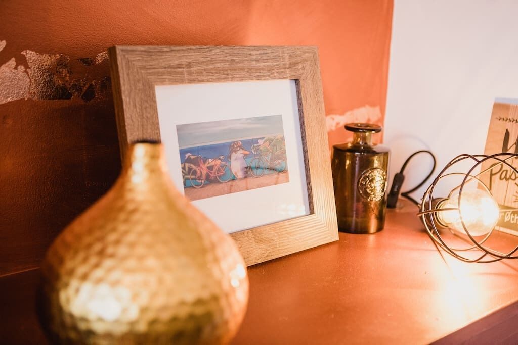 A framed picture on a wooden surface, a metallic bottle, and a wire-framed light bulb.