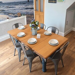 A dining area with a wooden table, grey chairs, and a view of the ocean through a window.