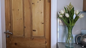 Une porte en bois, et sur le plan de travail de la cuisine, un vase en verre contenant des fleurs blanches.