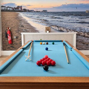 Une table de billard avec des billes, un extincteur et un décor représentant une plage.