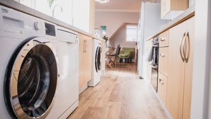 Un espace buanderie équipé d’un lave-linge et d’un sèche-linge, avec des placards en bois, et donnant sur un coin repas comprenant une table et des chaises.