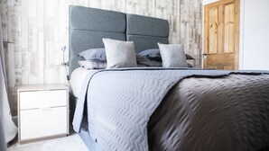 Un lit bien fait, avec une tête de lit grise, une table de chevet en bois et une porte en bois.