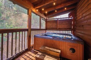 A wooden cabin with a hot tub, large windows, and a deck.