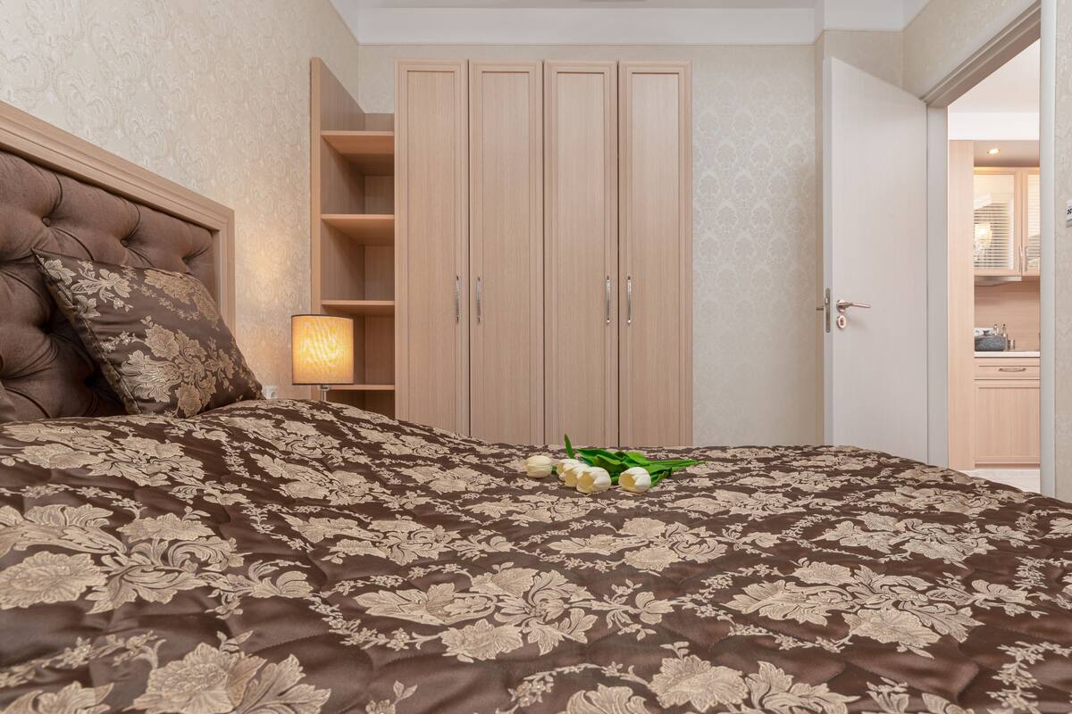 A bedroom with a large bed, a wardrobe, and a nightstand with a lamp.
