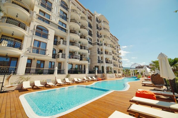 Un hotel con zona de piscina, varios balcones y sillones de sol.