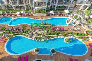Un complexe hôtelier doté de plusieurs piscines, de chaises longues et d’une fontaine centrale.