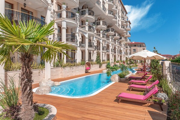 A luxurious hotel with a swimming pool, wooden deck, and lounge chairs.