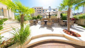 An outdoor patio area with wicker furniture, palm trees, and a central umbrella.