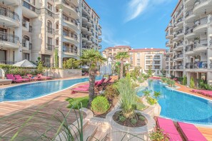 Un resort con una piscina central rodeada de zonas de descanso y vegetación.