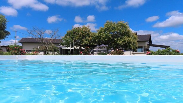 A swimming pool with a clear blue water surface, surrounded by a white pool deck. In the background, there are houses with a modern architectural style, featuring flat roofs and large windows.