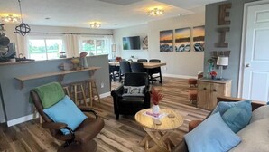 Un vaste espace de vie doté d’un plancher en bois, d’un canapé, d’un fauteuil, d’une table à manger et d’un coin cuisine avec une fenêtre.