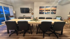 Une salle de conférence avec une longue table, des chaises noires, un téléviseur à écran plat et trois tableaux représentant des couchers de soleil accrochés au mur.