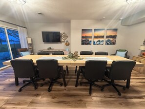 A conference room with a long table, black chairs, a flat-screen TV, and three sunset paintings on the wall.