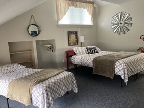 A bedroom with two beds, a window with curtains, a wall clock, a mirror, and a small shelf.