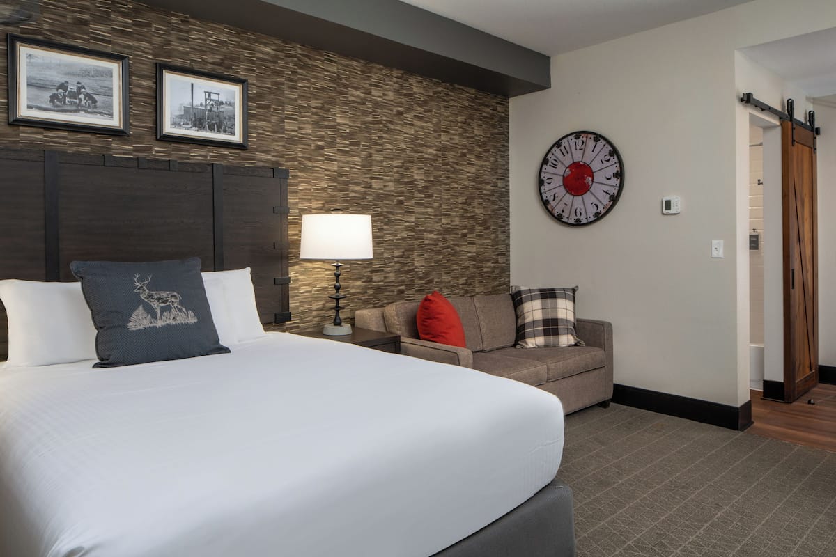 Una habitación de hotel con una cama grande, un sofá, un reloj en la pared y cuadros enmarcados sobre el sofá.