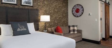 Ein Hotelzimmer mit einem großen Bett, einem Sofa, einer Wanduhr und gerahmten Bildern über dem Sofa.