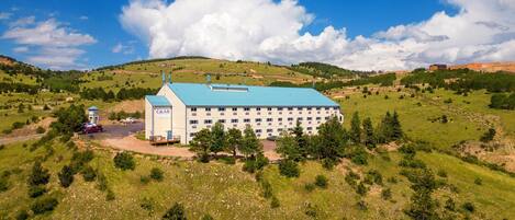 A large building with a blue roof, surrounded by green hills and trees.