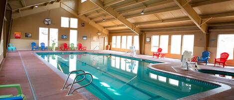 Una piscina interior con múltiples carriles, rodeada de sillas coloridas y un techo alto con vigas a la vista.