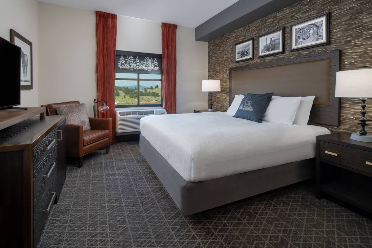 Una habitación de hotel con una cama grande, un escritorio, una silla y una ventana con cortinas.