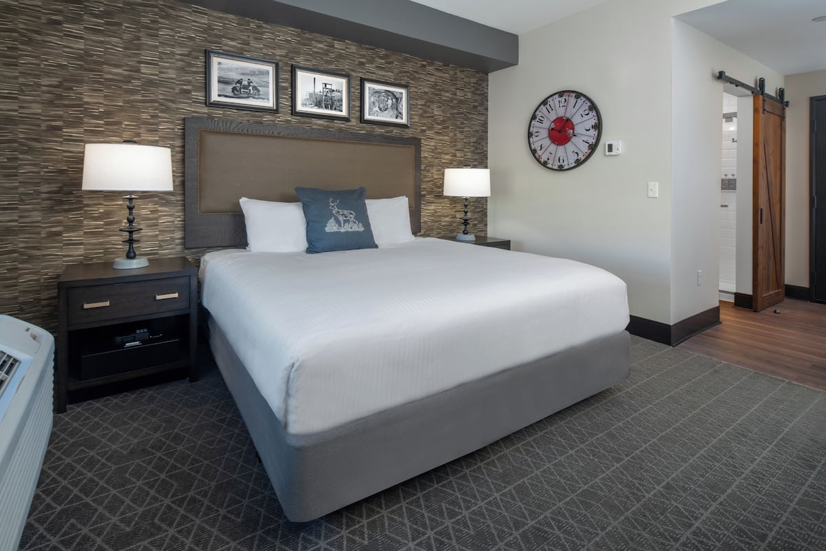 Habitación de hotel con una cama grande, dos mesitas de noche con lámparas, un reloj en la pared y una alfombra estampada.