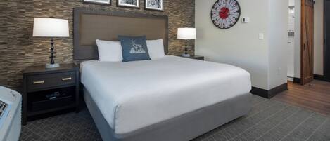 A hotel room with a large bed, two bedside tables with lamps, a clock on the wall, and a patterned carpet.