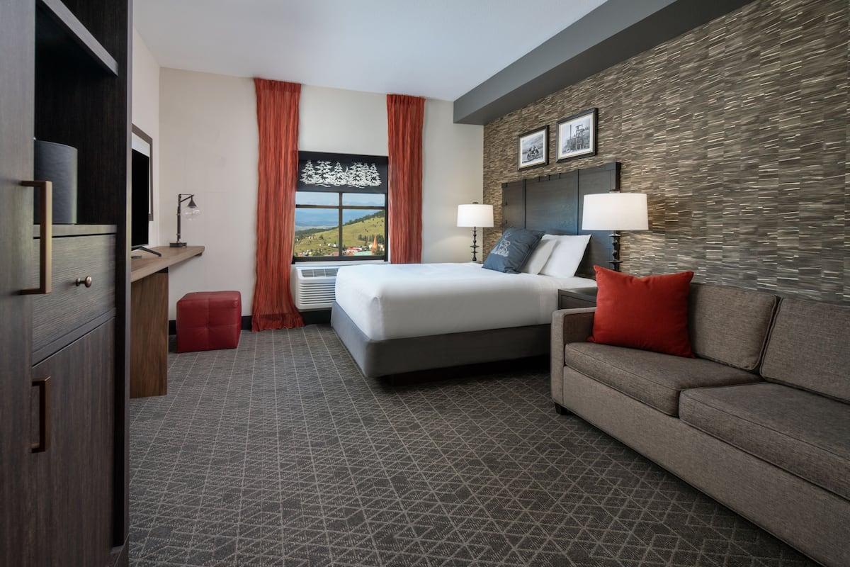 Una habitación de hotel con cama, sofá, escritorio y ventana con cortinas.