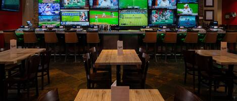 A sports bar with multiple screens displaying various sports events, wooden tables, and bar stools.