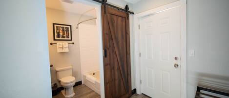 A bathroom with a toilet, bathtub, and a sliding barn-style door.