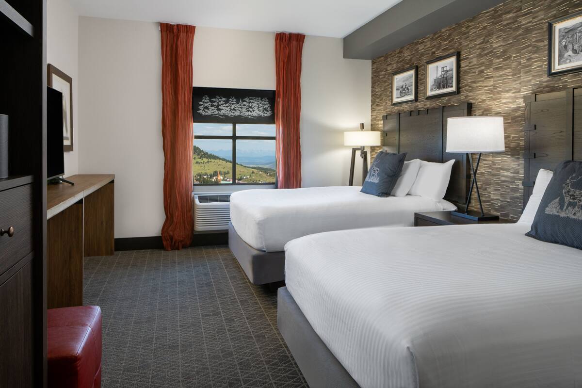 Habitación de hotel con dos camas, un escritorio, una silla, una ventana con vistas y una lámpara.