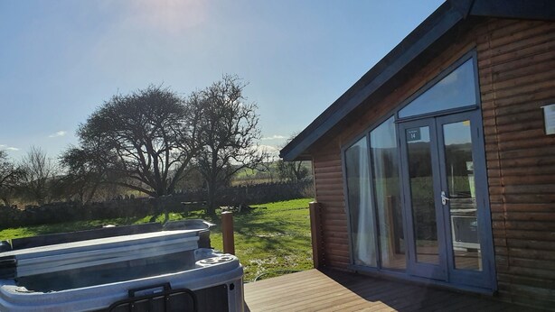 A wooden cabin with a hot tub on a wooden deck, large sliding glass doors, and a clear view of the surrounding landscape. - Log Cabin in the Clwydian Range (Ruthin)