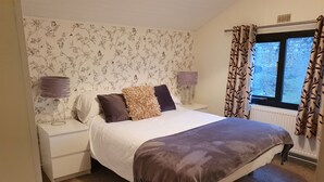 A bedroom with a bed, nightstands, a window with curtains, and a floral wallpaper. - Log Cabin in the Clwydian Range (Ruthin)