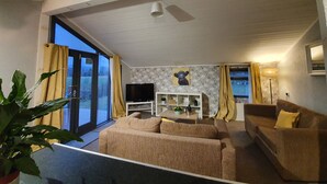 A living room with a sofa, a TV, a plant, and a window with curtains. - Log Cabin in the Clwydian Range (Ruthin)