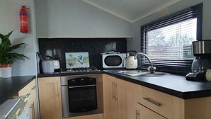 A compact kitchen with a microwave, kettle, sink, and dishwasher. - Log Cabin in the Clwydian Range (Ruthin)
