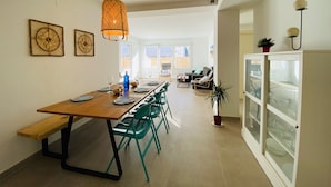Un comedor con una larga mesa de madera, sillas verdes y una lámpara colgante.