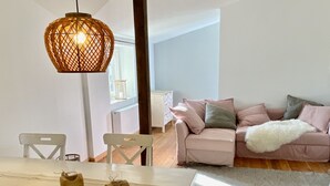 Una sala de estar moderna con un sofá blanco, una mesa de comedor con sillas y una lámpara colgante.