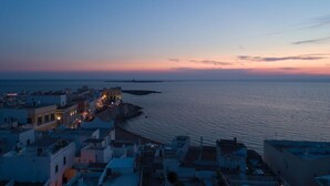A coastal town at dusk with buildings along the waterfront and a prominent structure with lights. - Palazzo Colombo (Gallipoli)