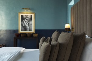 Un dormitorio con cama, almohadas, una mesita de noche con lámpara y una obra enmarcadas en la pared.