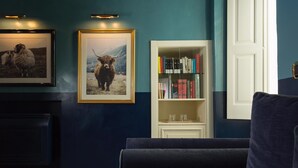 A room with a dark blue wall, a bookshelf with books, a framed picture of a yak, and a dark blue sofa. - Palazzo Colombo (Gallipoli)