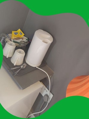 Eine Küchenzeile mit einem weißen Wasserkocher, zwei weißen Tassen und einem Löffel auf einer grauen Arbeitsplatte.