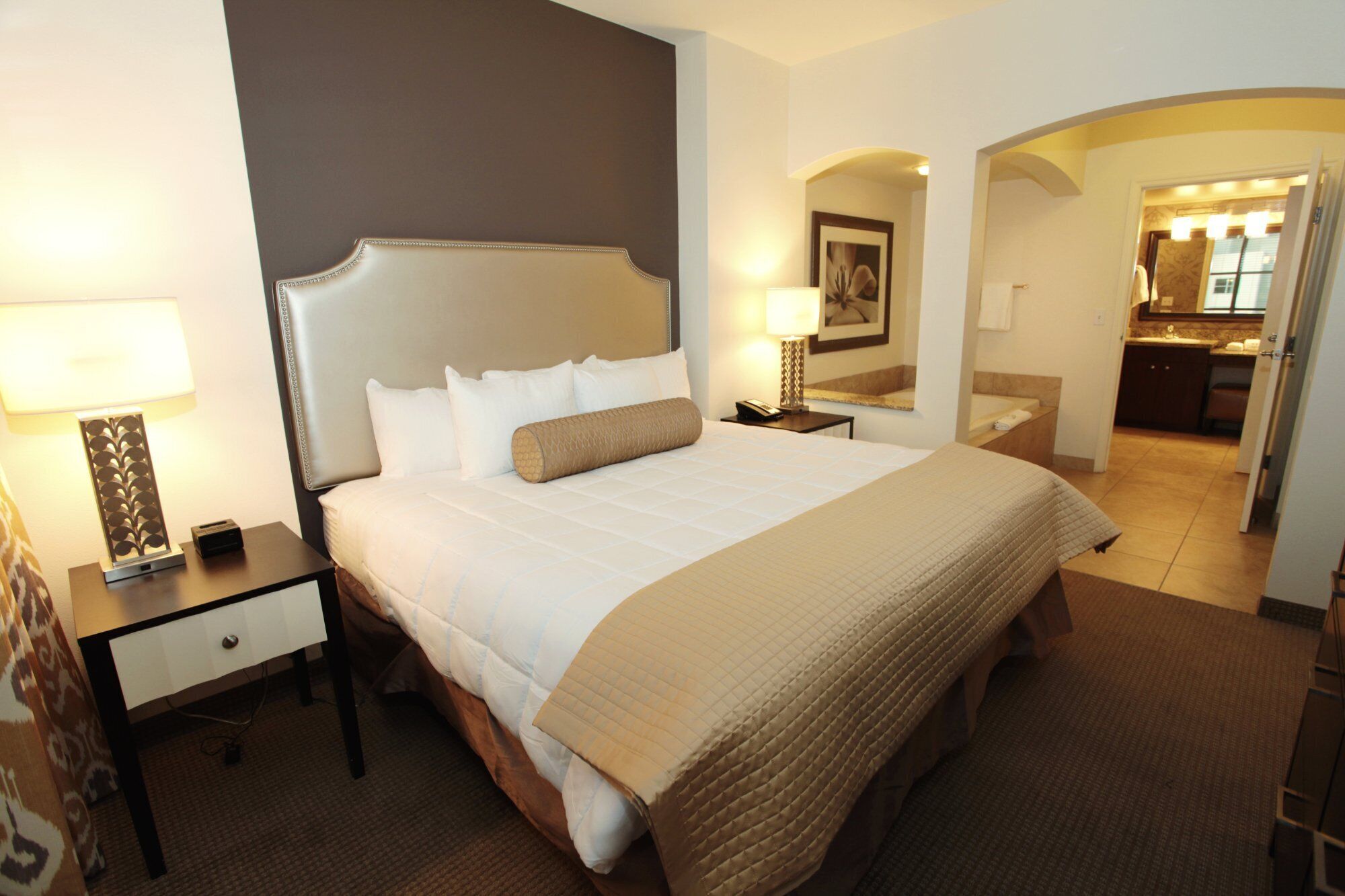 A hotel room with a large bed, bedside tables, a desk, and a bathroom visible through an archway.