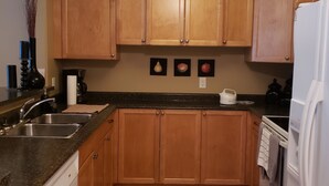 A kitchen with wooden cabinets, a granite countertop, a white dishwasher, a white refrigerator, and a ceiling light. - Quiet condo at beautiful Mabel Lake (Enderby)